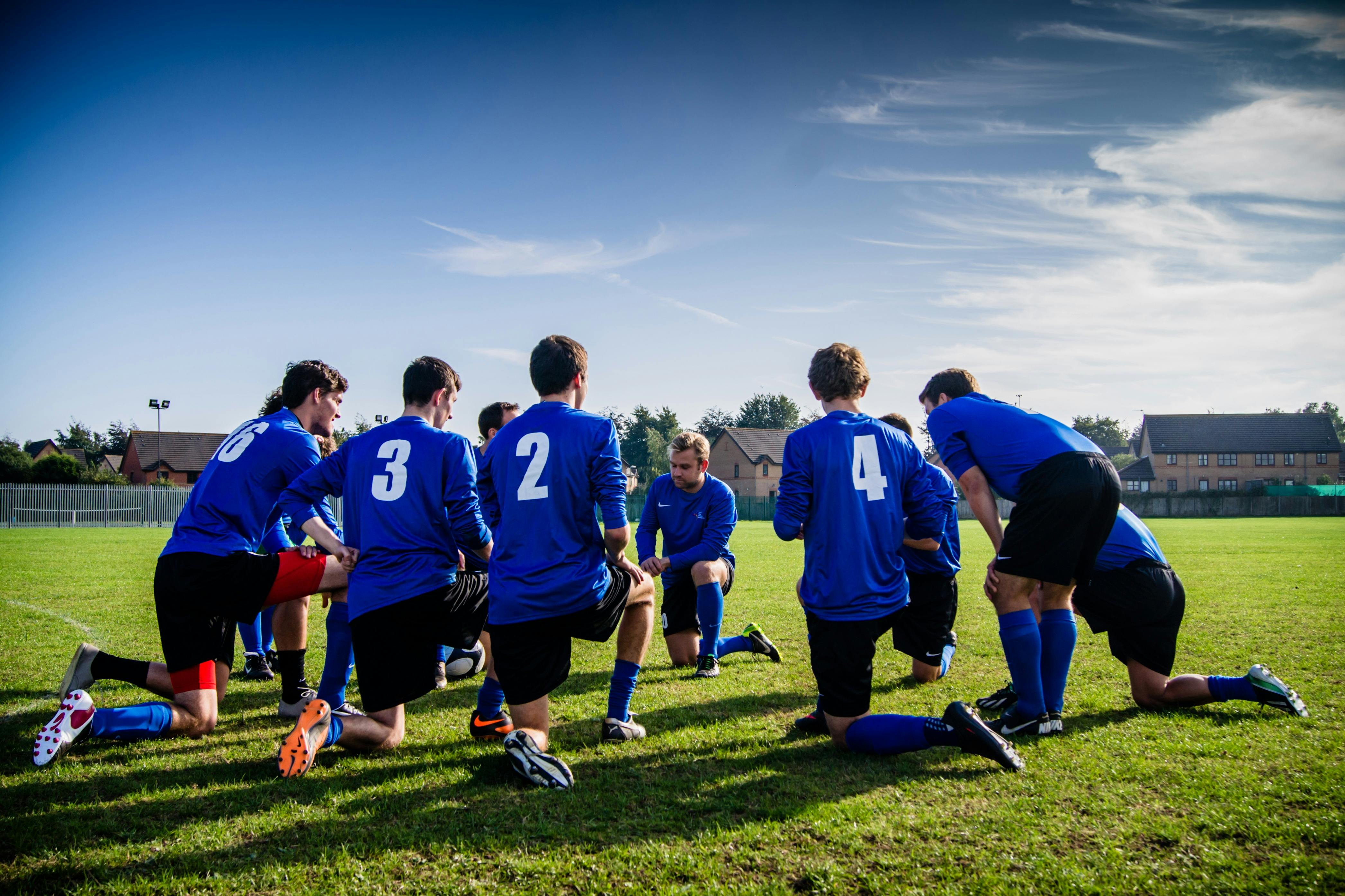 Football team kneeling on pitch in circle together.
